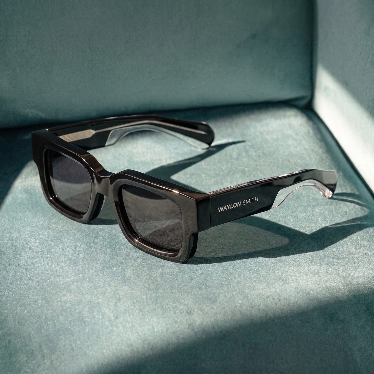 Black Waylon Smith sunglasses resting on a teal velvet surface, studio product shot