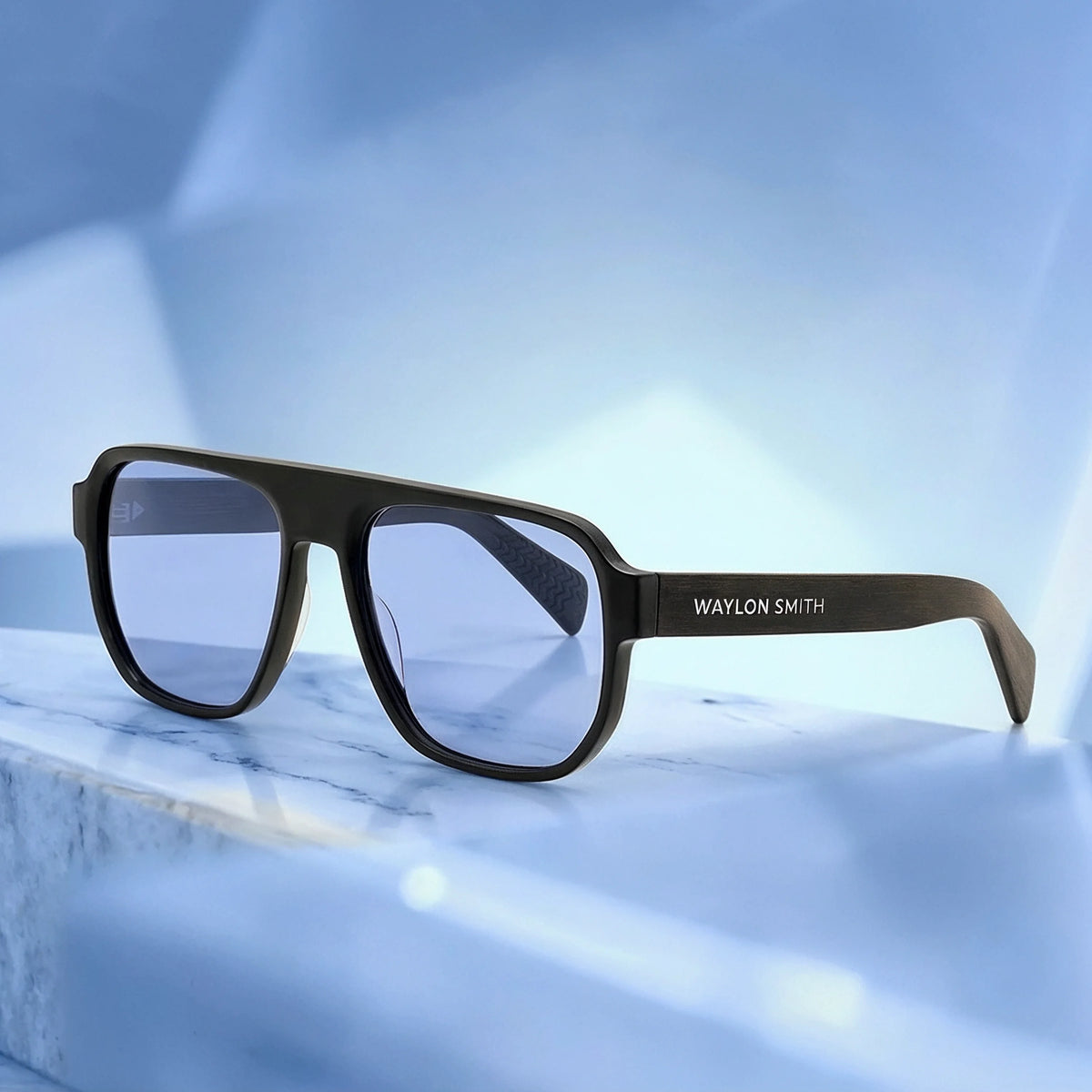 Black Waylon Smith sunglasses with blue lenses resting on a marble surface, showing the Waylon Smith wordmark on the temple