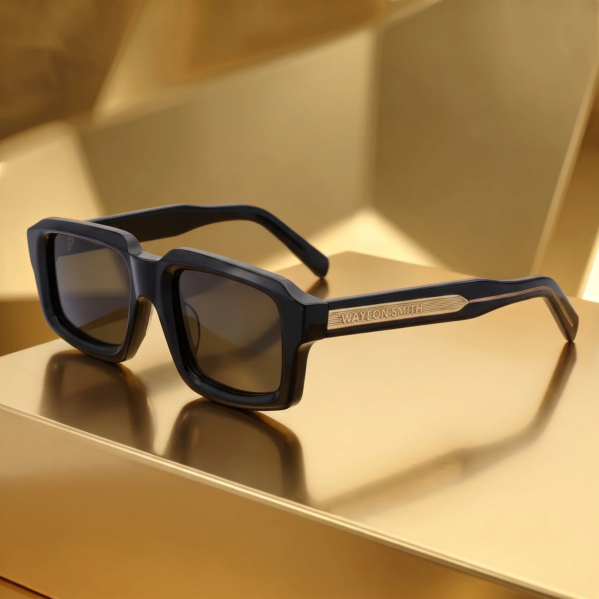 Black Waylon Smith sunglasses resting on a gold surface, showing the Waylon Smith wordmark on the temple