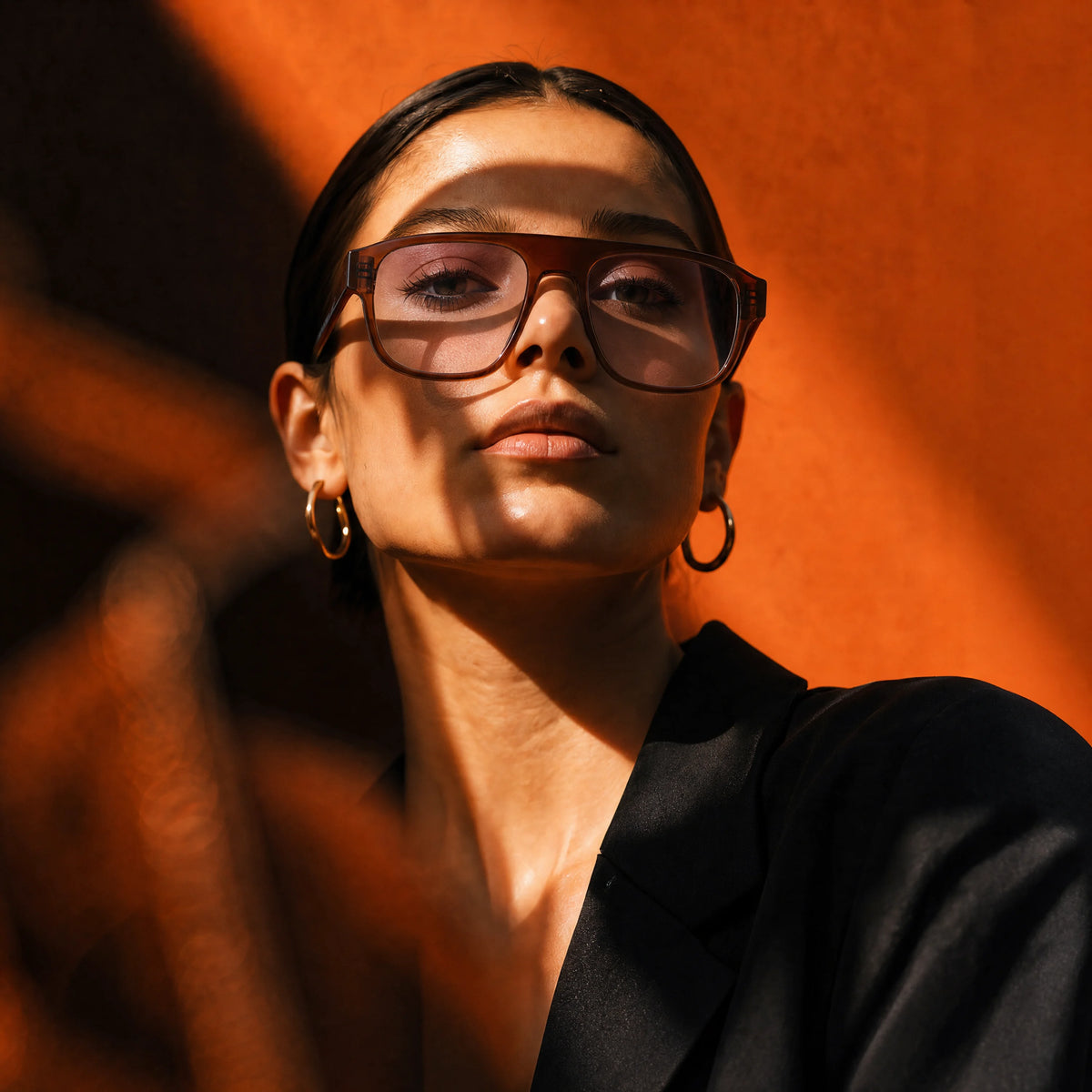 Close-up portrait of a woman wearing tortoiseshell Waylon Smith sunglasses against a warm orange backdrop