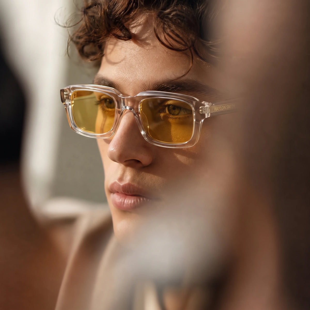 Close-up portrait of a man wearing transparent Waylon Smith Syndicate sunglasses with amber lenses, showing the Waylon Smith wordmark on the temple
