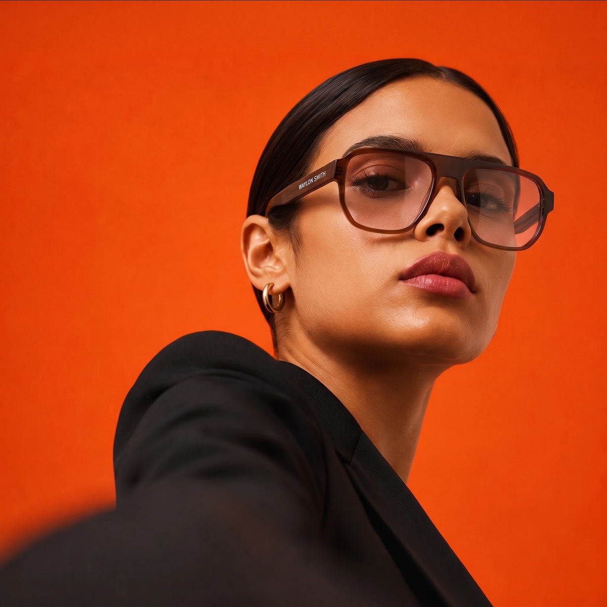 Woman in a black blazer wearing amber tortoiseshell Waylon Smith sunglasses against an orange background