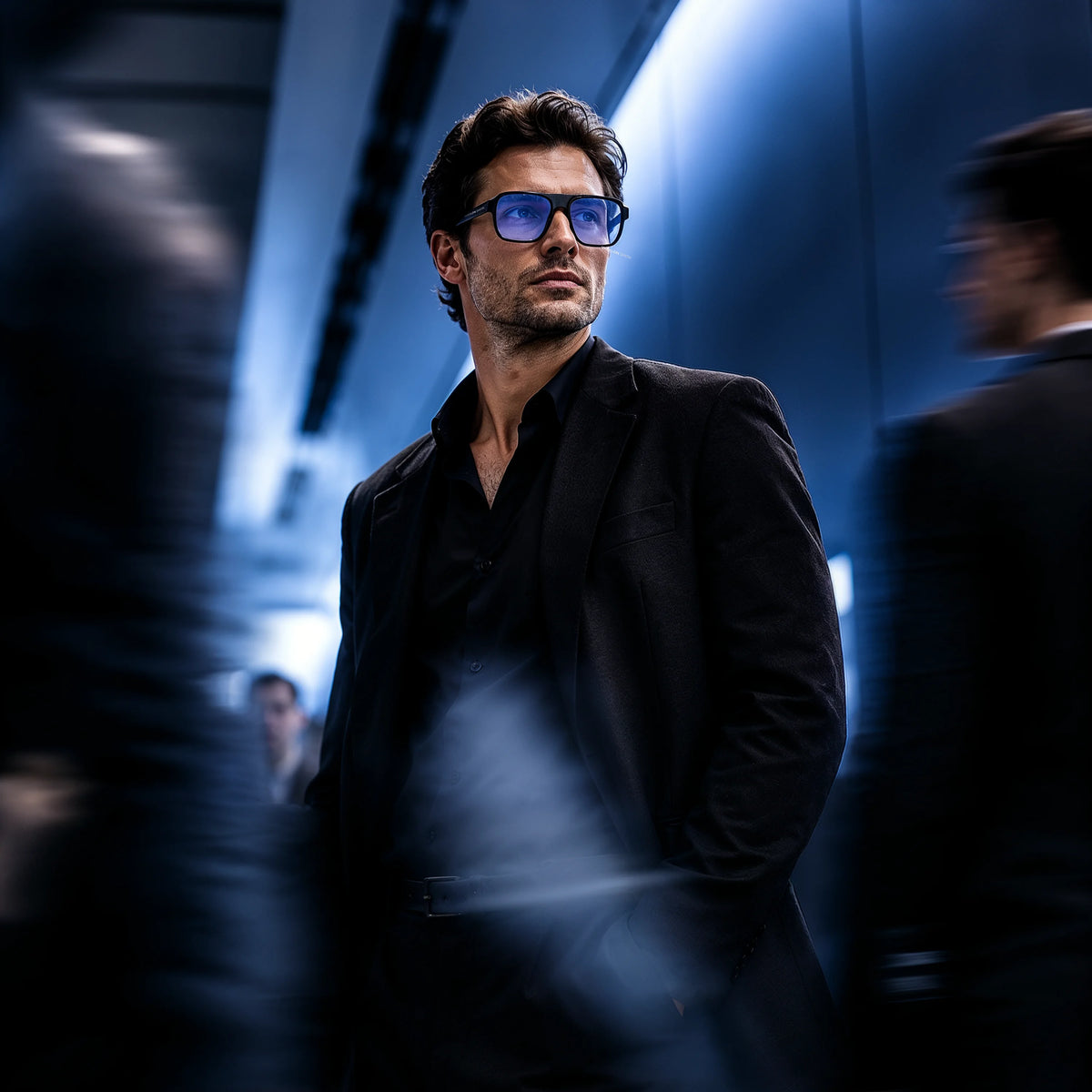 Man in a black suit wearing black Waylon Smith sunglasses with blue lenses in a dimly lit corridor