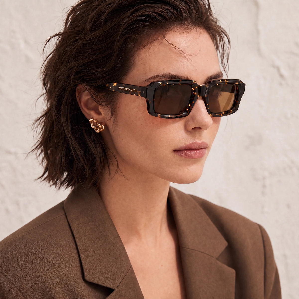 Close-up portrait of a woman wearing tortoiseshell Waylon Smith sunglasses against a textured wall