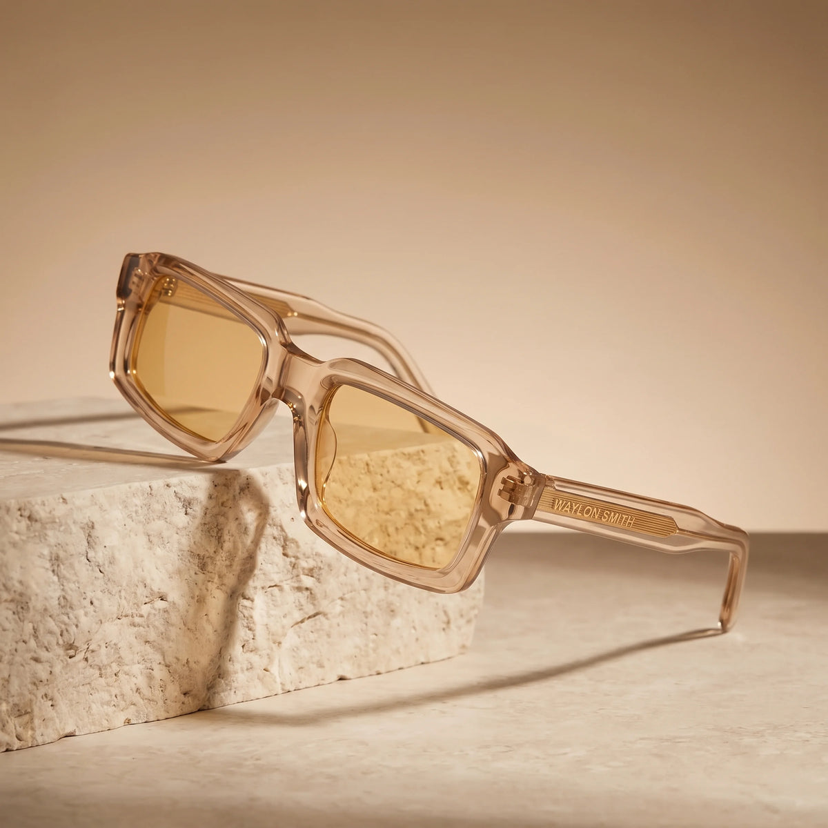 Waylon Smith Syndicate sunglasses in Translucent Amber, studio product shot resting on a stone pedestal