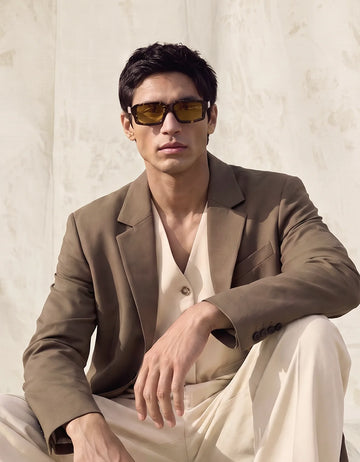 Man in a beige suit wearing amber-tinted Waylon Smith Syndicate sunglasses, seated portrait
