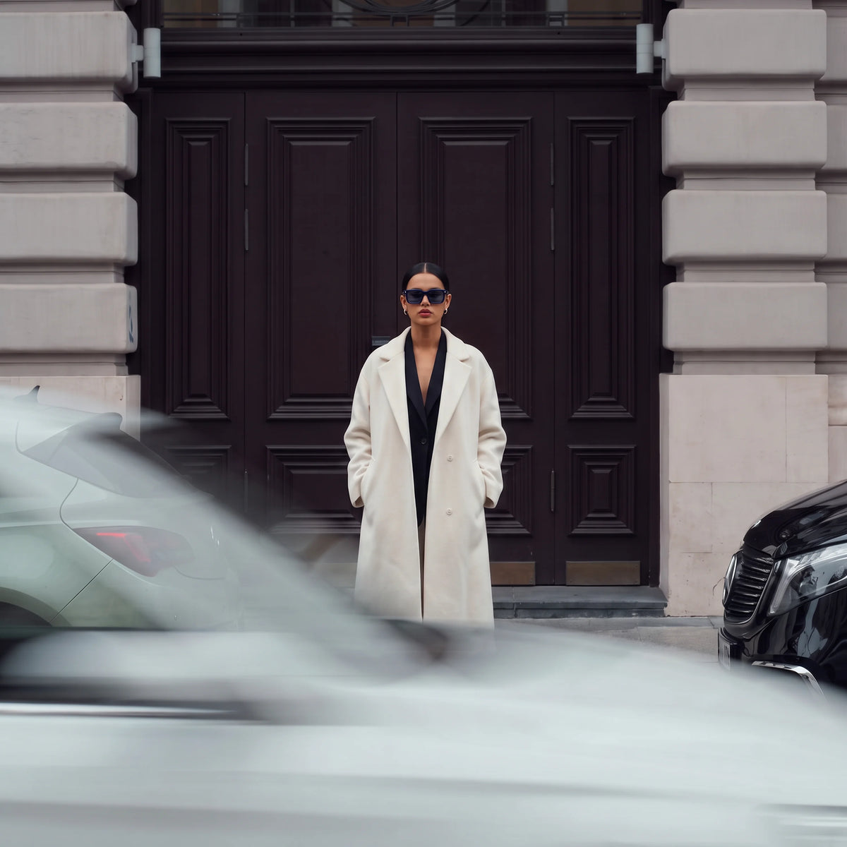 Woman in a beige coat wearing Waylon Smith Vinewood sunglasses in blue on an urban street